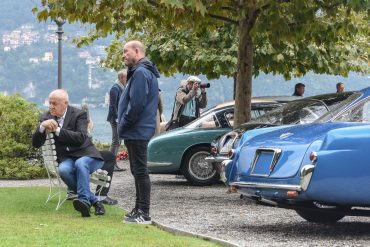 Man sitting on bench at Villa d'Este near the shore of Lake Como in Italy with parked cars nearby