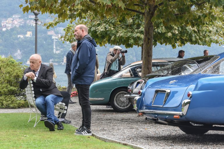 Man sitting on bench at Villa d'Este near the shore of Lake Como in Italy with parked cars nearby