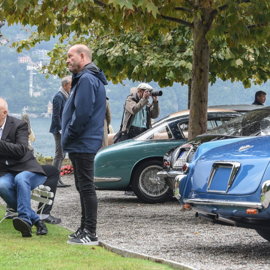 Man sitting on bench at Villa d'Este near the shore of Lake Como in Italy with parked cars nearby