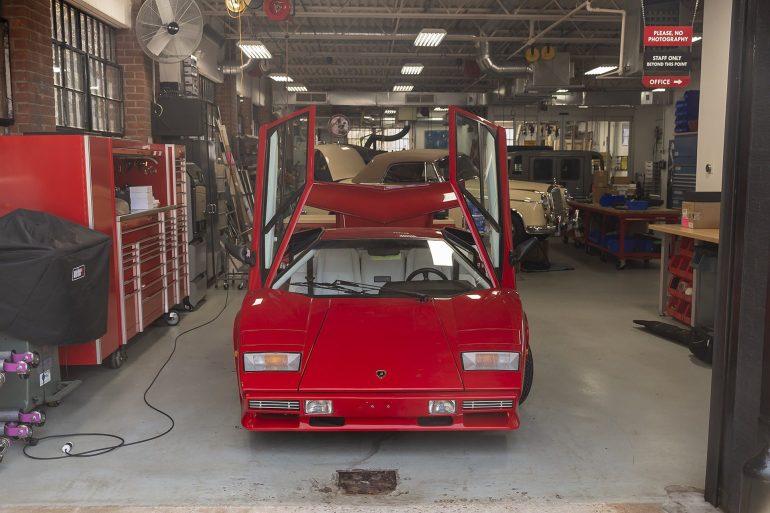 Red sports car with vertical doors raised in Ai Design shop